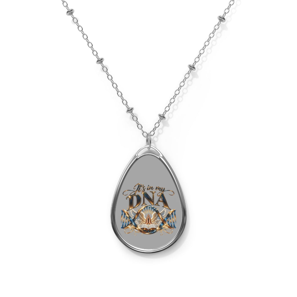 Silver-tone elliptical Christian pendant necklace featuring It's in My DNA gold-and-blue artwork with intertwined DNA strands, praying hands, decorative wings, and an open Bible on a gray background.