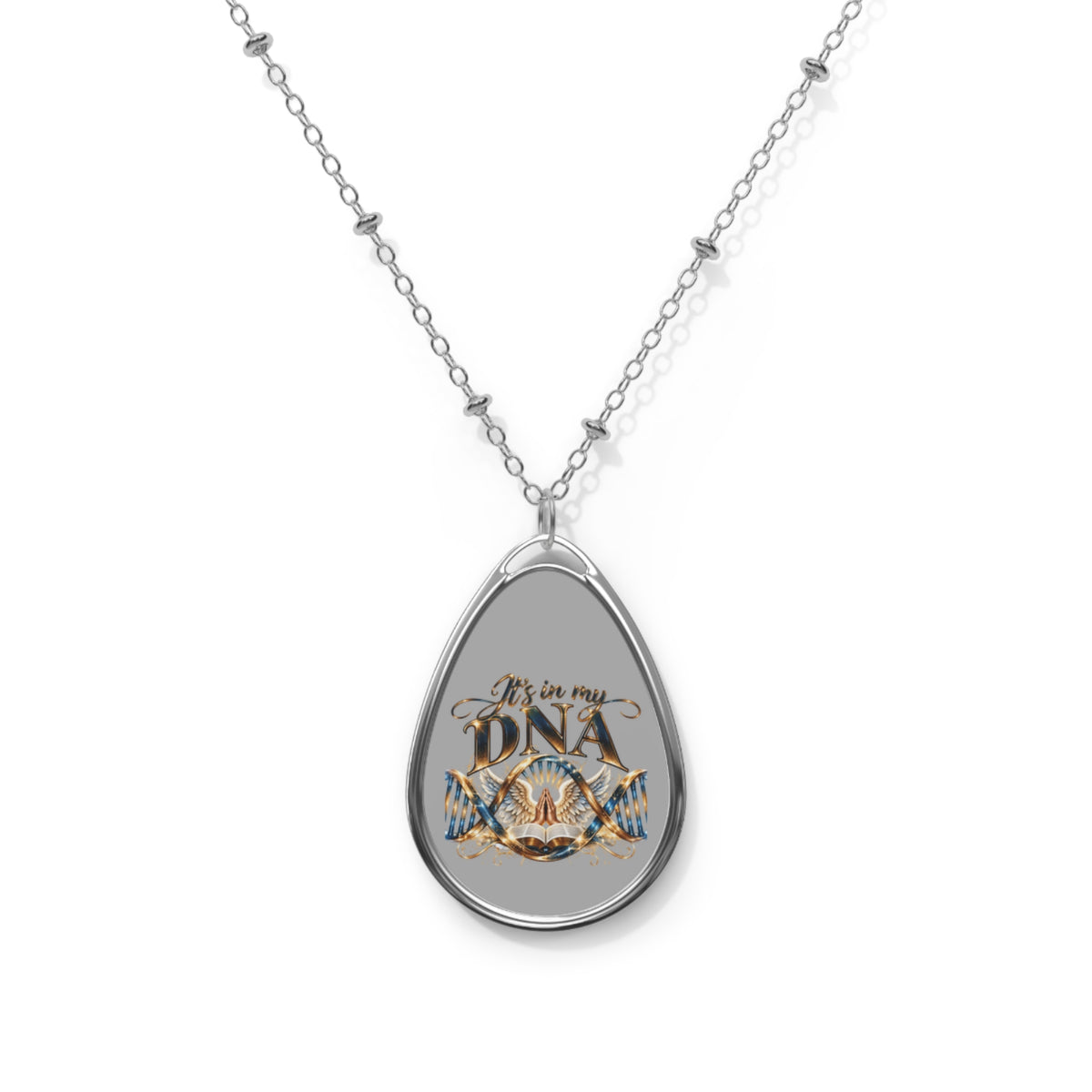 Silver-tone elliptical Christian pendant necklace featuring It's in My DNA gold-and-blue artwork with intertwined DNA strands, praying hands, decorative wings, and an open Bible on a gray background.
