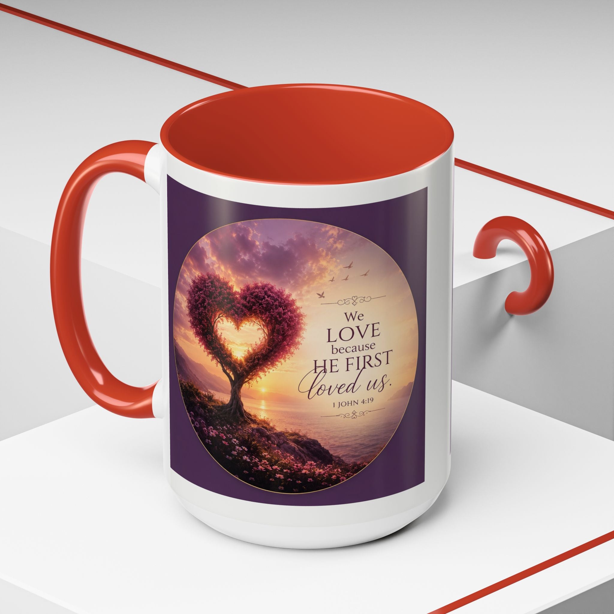 Inspirational Christian coffee mug featuring a glowing heart-shaped tree at sunset with the scripture “We Love Because He First Loved Us” from 1 John 4:19 and contrasting black handle and interior.