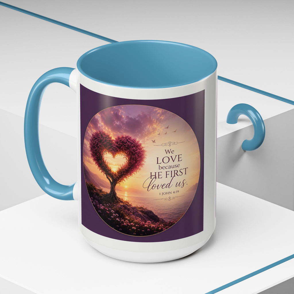 Inspirational Christian coffee mug featuring a glowing heart-shaped tree at sunset with the scripture “We Love Because He First Loved Us” from 1 John 4:19 and contrasting black handle and interior.