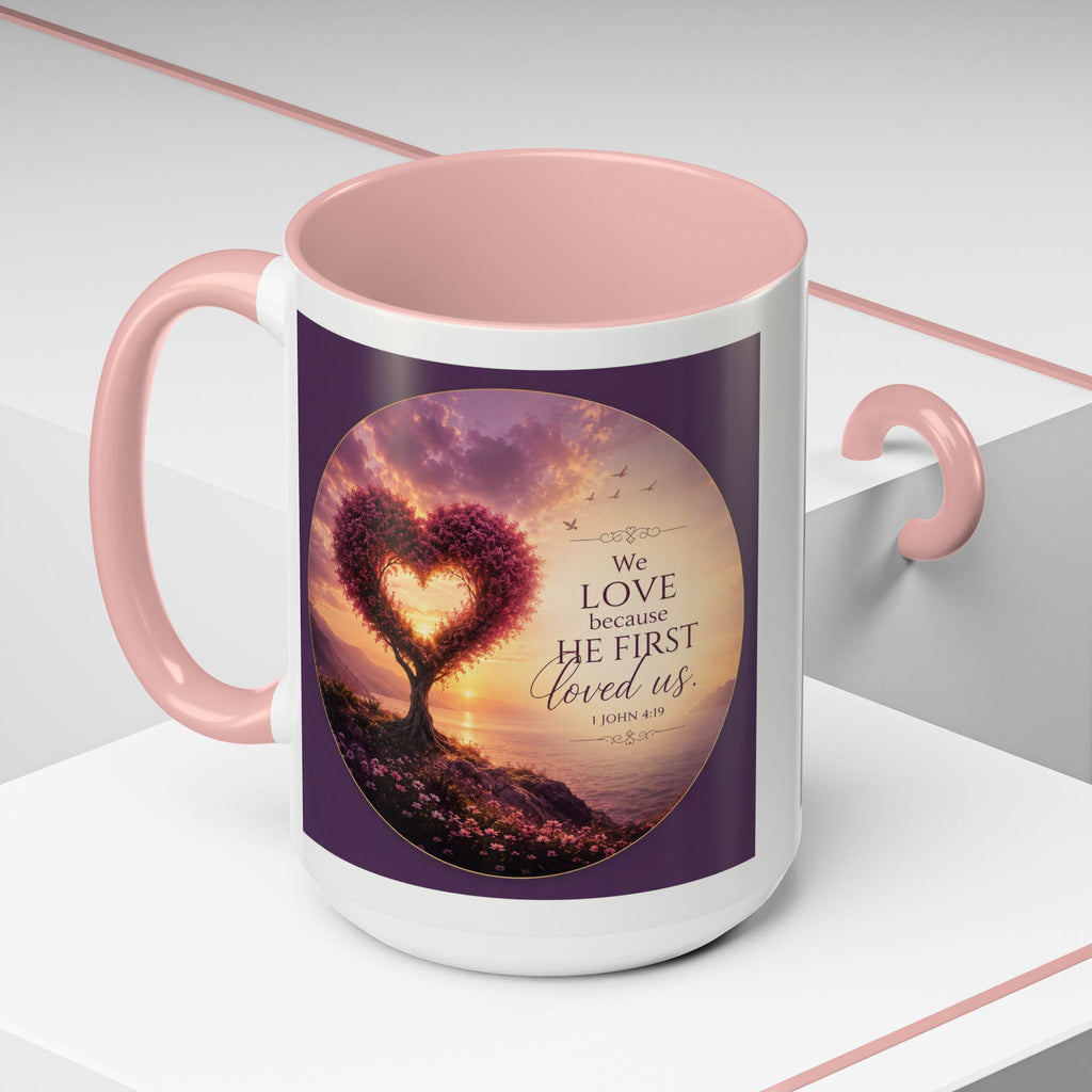 Inspirational Christian coffee mug featuring a glowing heart-shaped tree at sunset with the scripture “We Love Because He First Loved Us” from 1 John 4:19 and contrasting black handle and interior.